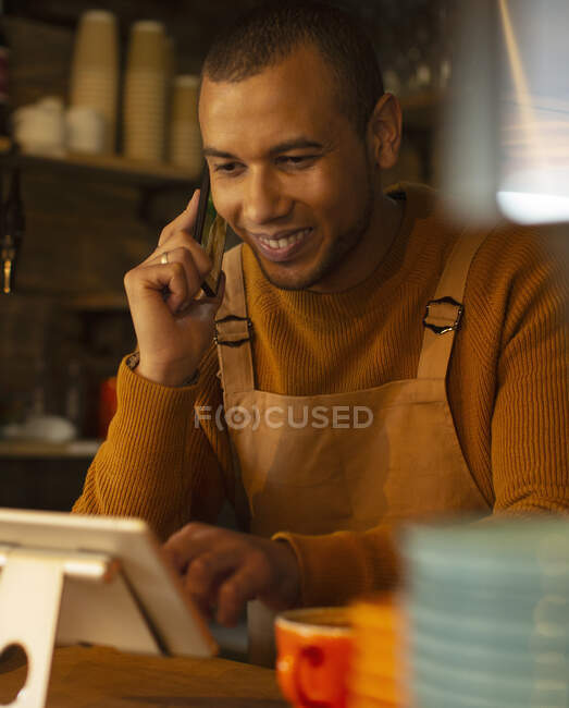 Усміхнений чоловік-бариста приймає замовлення по телефону в цифровому планшеті в кафе — стокове фото