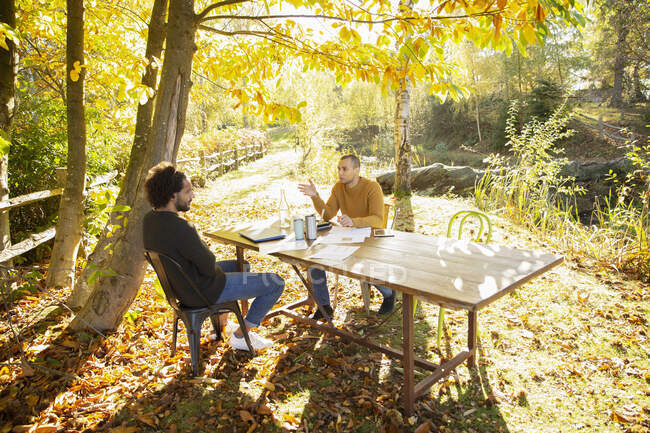 Des hommes d'affaires réunis à table dans un parc d'automne idyllique ensoleillé — Photo de stock