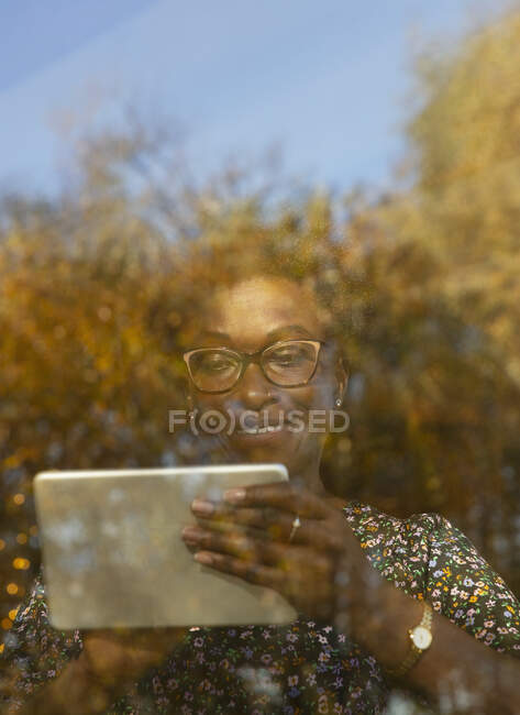 Улыбающаяся женщина с цифровым планшетом в солнечном осеннем окне — стоковое фото