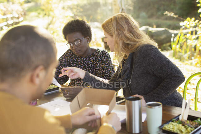 Businesswomen discussing paperwork and eating lunch at table in park — Stock Photo