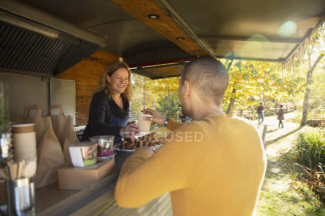 Friendly food cart owner serving coffee to customer in autumn park — Stock Photo