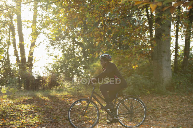 Donna felice in bicicletta tra le foglie autunnali nel parco soleggiato — Foto stock