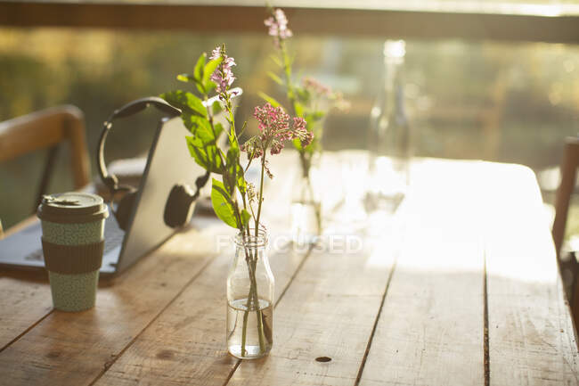 Простое расположение полевых цветов в стеклянной бутылке на деревенском столике кафе — стоковое фото