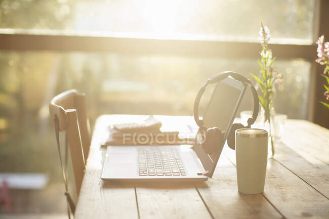 Auriculares, ordenador portátil y café en la mesa de café soleado - foto de stock
