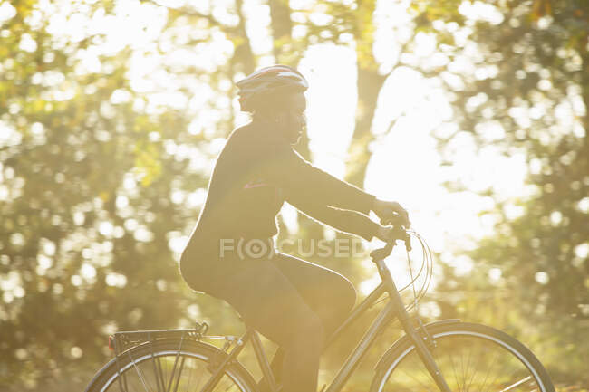 Woman in helmet riding bicycle in sunny autumn park — Stock Photo