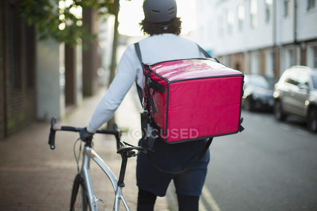 Mensajero de bicicleta masculina entrega de alimentos en la acera urbana - foto de stock