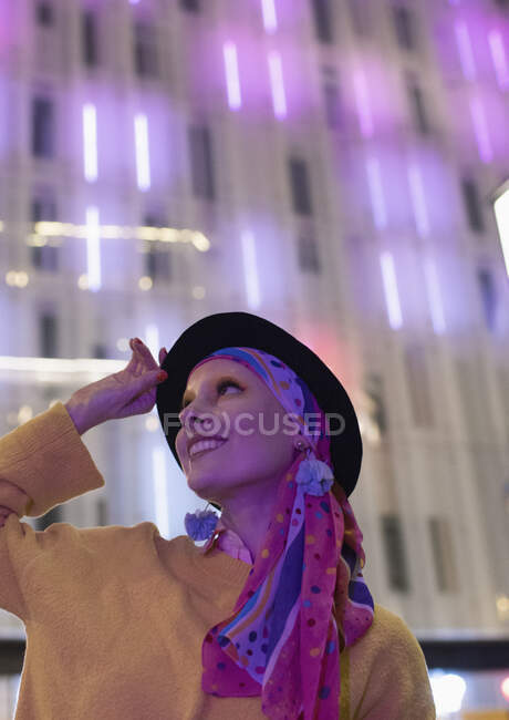 Portrait fashionable happy woman looking up at neon building — Stock Photo