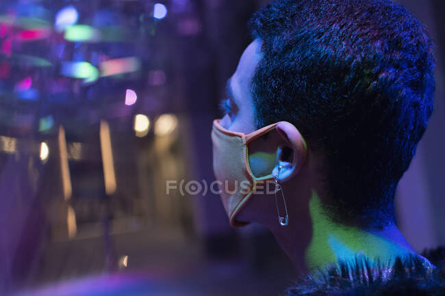 Jovem com brinco pino de segurança usando máscara facial em boate — Fotografia de Stock