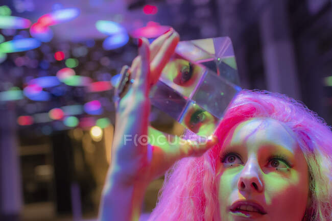 Woman with pink hair looking up at dimensional crystal cube — Stock Photo