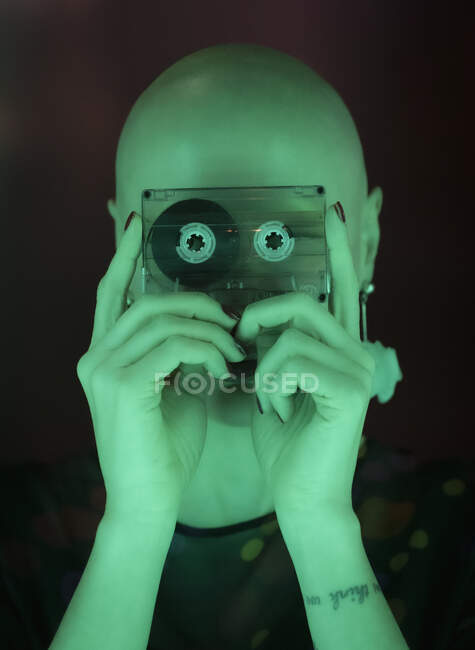 Porträt Frau mit rasiertem Kopf hält Kassettenband in grünem Licht — Stockfoto