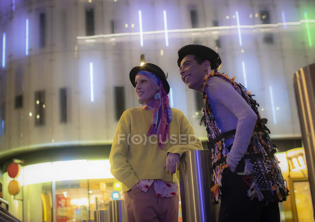 Fashionable couple below neon city building at night — Stock Photo