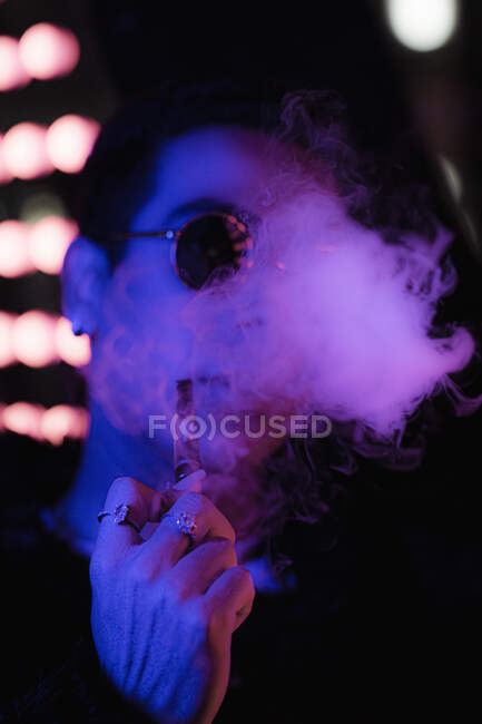 Portrait cool young man with vape pen blowing smoke in neon light — Stock Photo