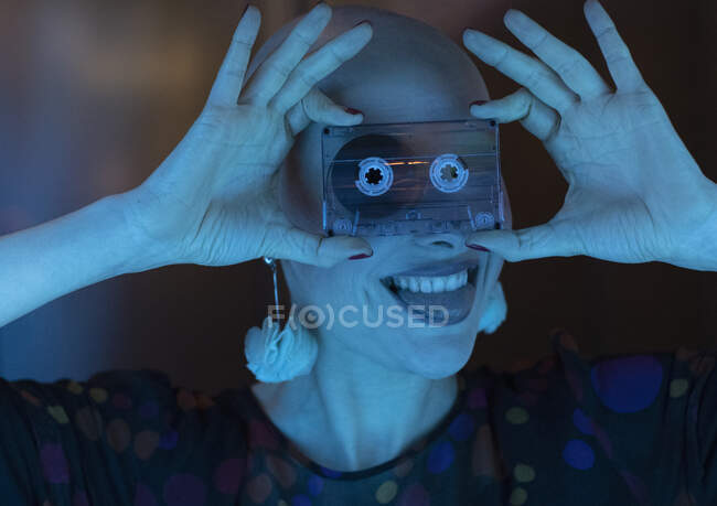 Portrait playful woman with shaved head holding cassette tape over face — Stock Photo