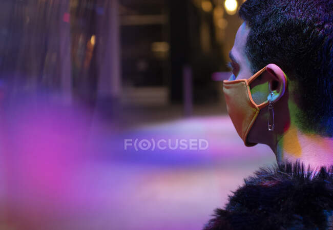 Elegante giovane uomo con orecchino spillo di sicurezza indossando maschera sotto al neon — Foto stock