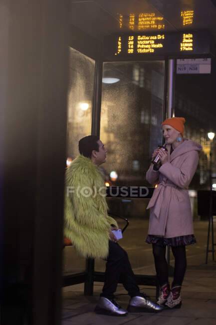 Стильная молодая пара разговаривает на городской автобусной остановке ночью — стоковое фото