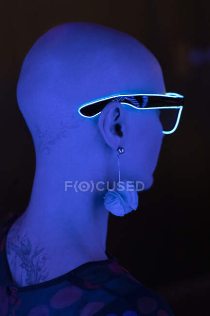 Stylische Frau mit rasiertem Kopf trägt Neon-Brille im Blaulicht — Stockfoto