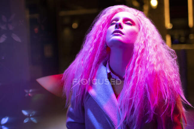 Hermosa mujer con el pelo rosa y la cabeza hacia atrás bajo la luz - foto de stock