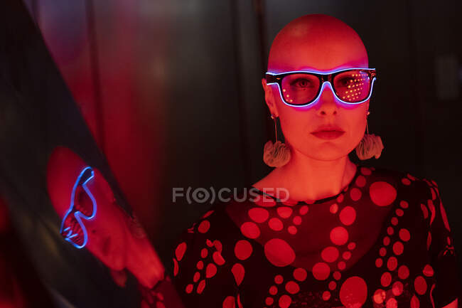 Ritratto donna fresca con testa rasata e occhiali al neon a luce rossa — Foto stock