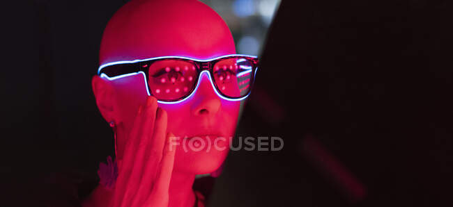 Porträt stilvolle Frau mit rasiertem Kopf in Neon-Brille im Rotlicht — Stockfoto
