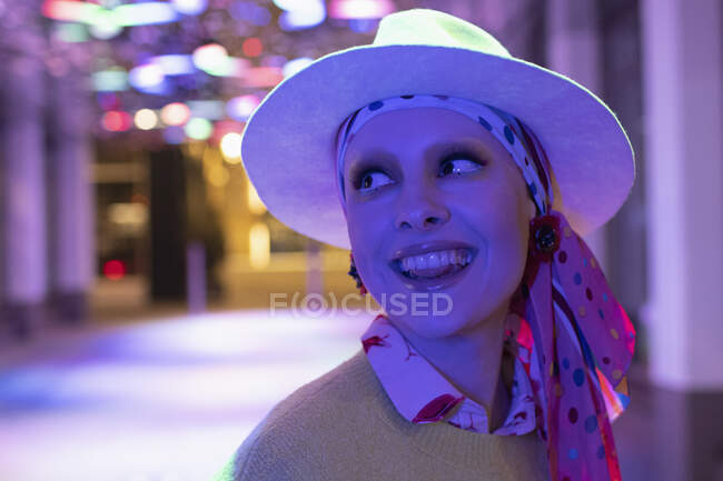 Portrait happy stylish woman in headscarf and fedora under neon light — Stock Photo