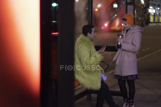 Couple élégant avec café parlant à l'arrêt de bus en ville la nuit — Photo de stock