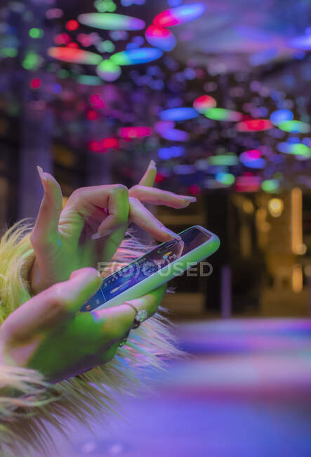 Cerca de la mujer que usa el teléfono inteligente en la discoteca bajo luces de neón - foto de stock