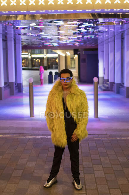 Portrait stylish young man in feather coat under neon city lights — Stock Photo