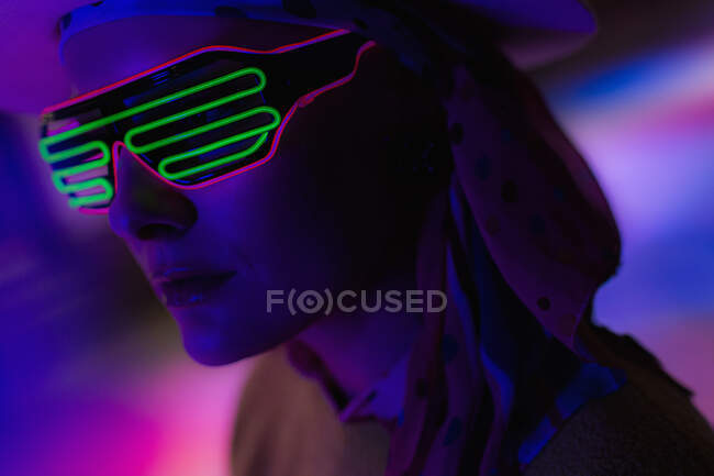 Close up stylish woman wearing neon sunglasses in dark — Stock Photo