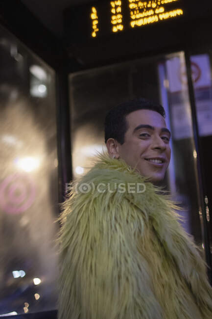 Portrait happy eccentric young man in feather coat at city bus stop — Stock Photo
