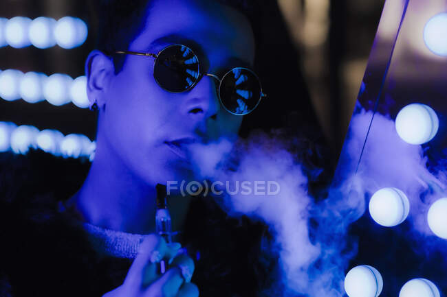 Portrait cool young man in sunglasses vaping in dark neon. nightclub — Stock Photo