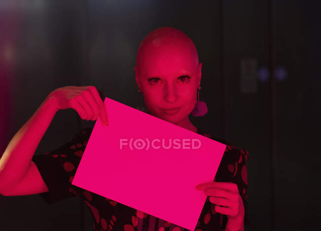 Porträt Frau mit rasiertem Kopf hält leeres Schild im Rotlicht — Stockfoto