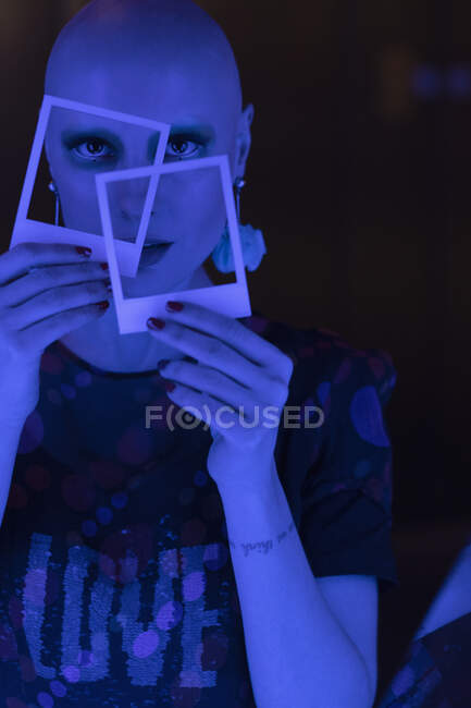 Portrait cool woman with shaved head holding polaroids in blue light — Stock Photo