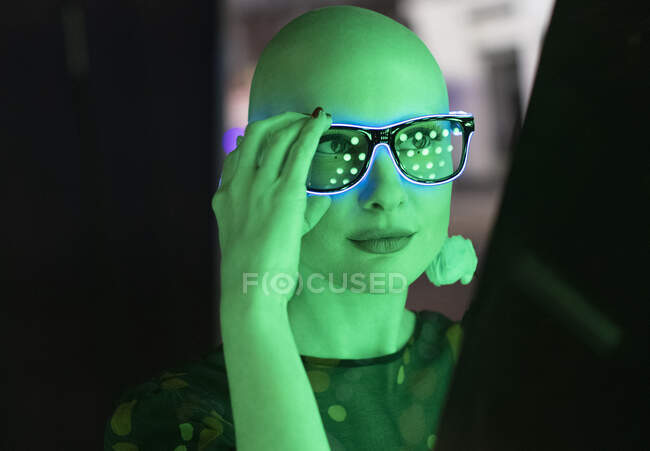 Porträt stilvolle Frau mit rasiertem Kopf in Neon-Brille in grünem Licht — Stockfoto