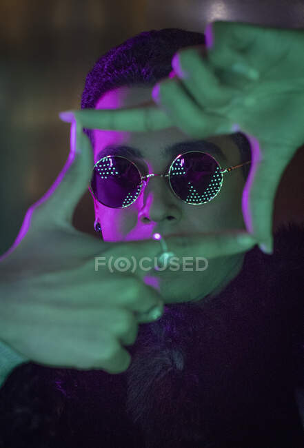 Портрет прохладный молодой человек в солнцезащитных очках, образующих рамку пальца в неоне — стоковое фото