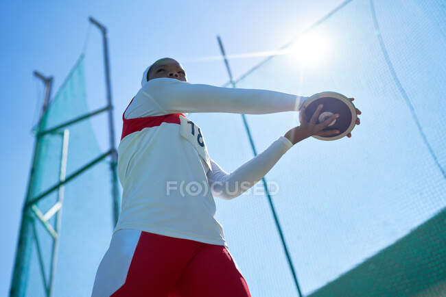 Female track and field athlete throwing discus under sunny blue sky — Stock Photo