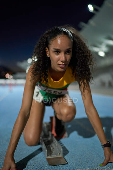 Determined female track and field athlete at starting block on track — Stock Photo