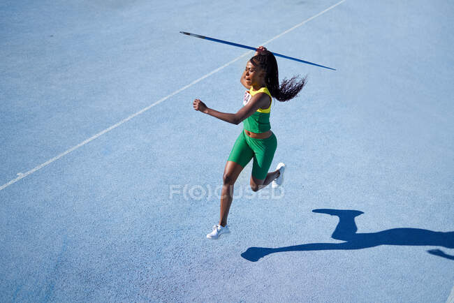 Feminino faixa e campo atleta jogando dardo na faixa azul ensolarado — Fotografia de Stock