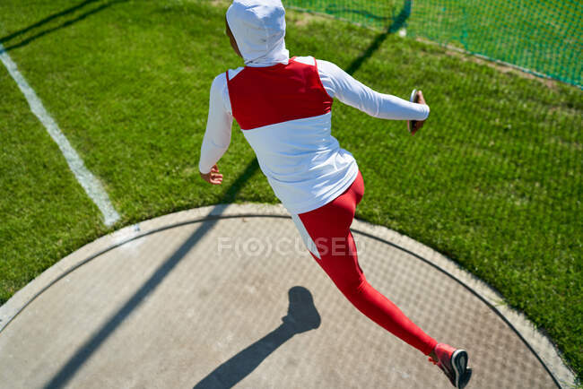 Female track and field athlete in hijab throwing discus — Stock Photo