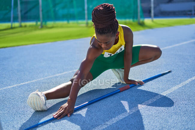 Atleta de pista y campo femenino con jabalina estirándose en pista soleada - foto de stock