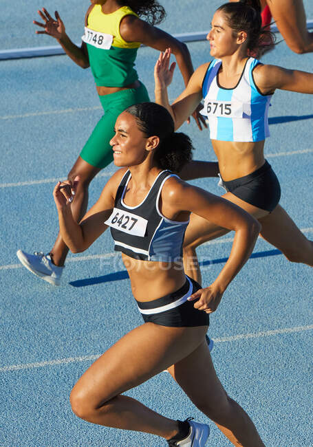 Female track and field athletes running on sunny track — Stock Photo