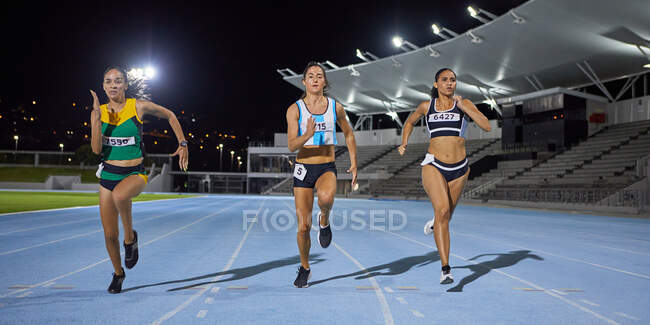 Atletas de pista e campo do sexo feminino que correm em competição na pista noturna — Fotografia de Stock