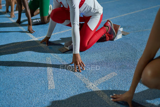 Female track and field athletes at starting line on blue track — Stock Photo