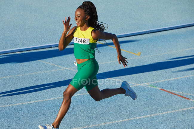 Smiling female track and field athlete running on sunny track — Stock Photo