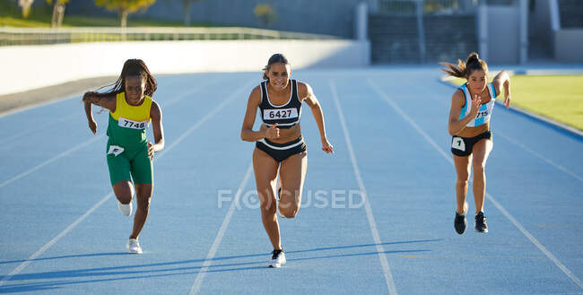 Female track and field athletes competing on sunny track — Stock Photo