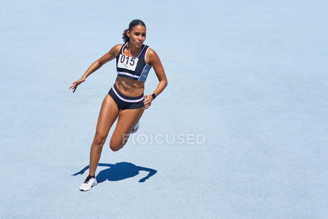Female track and field athlete on sunny blue track — Stock Photo