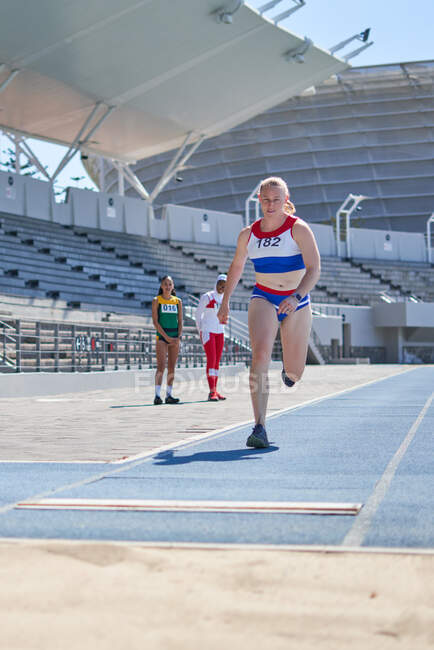 Feminino pista e campo atleta salto em comprimento na pista ensolarada — Fotografia de Stock