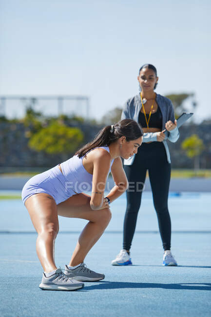 Atleta de atletismo femenino estirándose con entrenador en pista - foto de stock