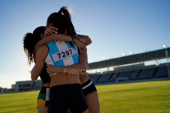 Feliz pista femenina y atletas de campo abrazándose en el estadio infield - foto de stock