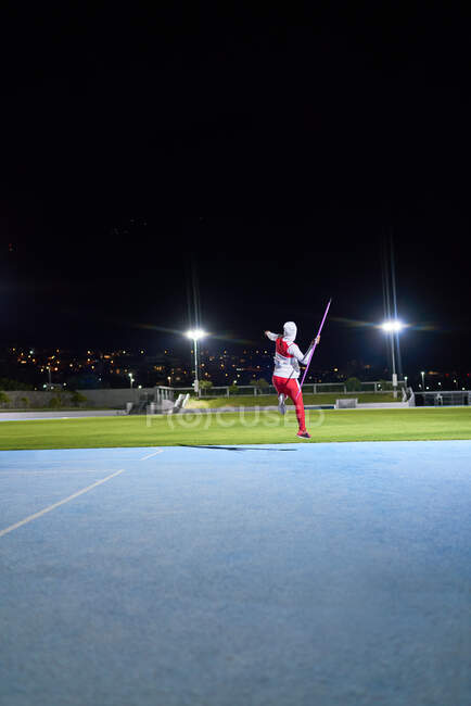 Feminino pista e campo atleta jogando dardo no estádio à noite — Fotografia de Stock