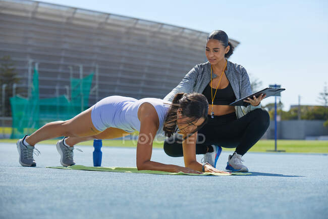Treinador ajudando atleta de atletismo feminino fazendo pranchas na pista — Fotografia de Stock